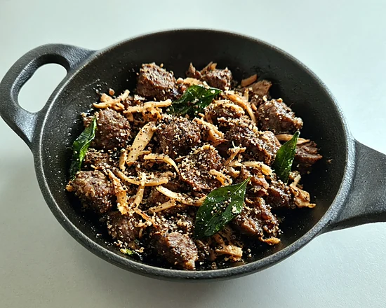 Beef coconut pepper fry with fried coconut slivers and curry leaves in a black iron pan