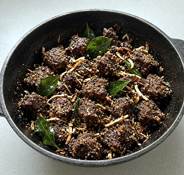 Beef coconut pepper fry with fried coconut slivers and curry leaves in a black iron pan